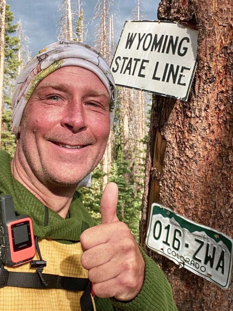 Boss smiling beside the Wyoming state line marker on trail
